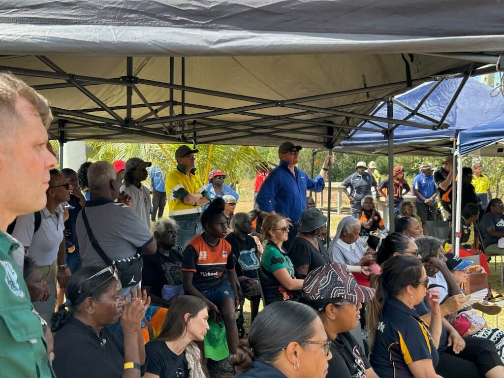 A crowd of people sitting under shade 