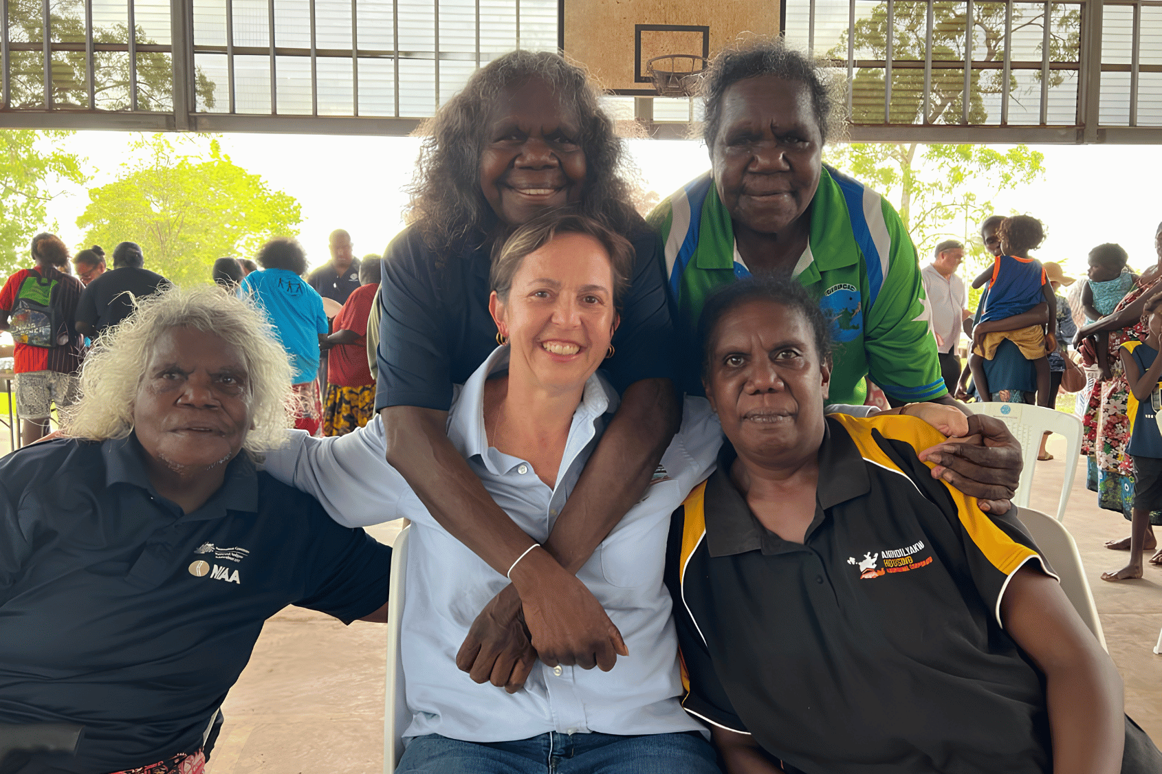 Five Women, three sitting side by side with arms around shoulders and 2 women standing embracing the women sitting.